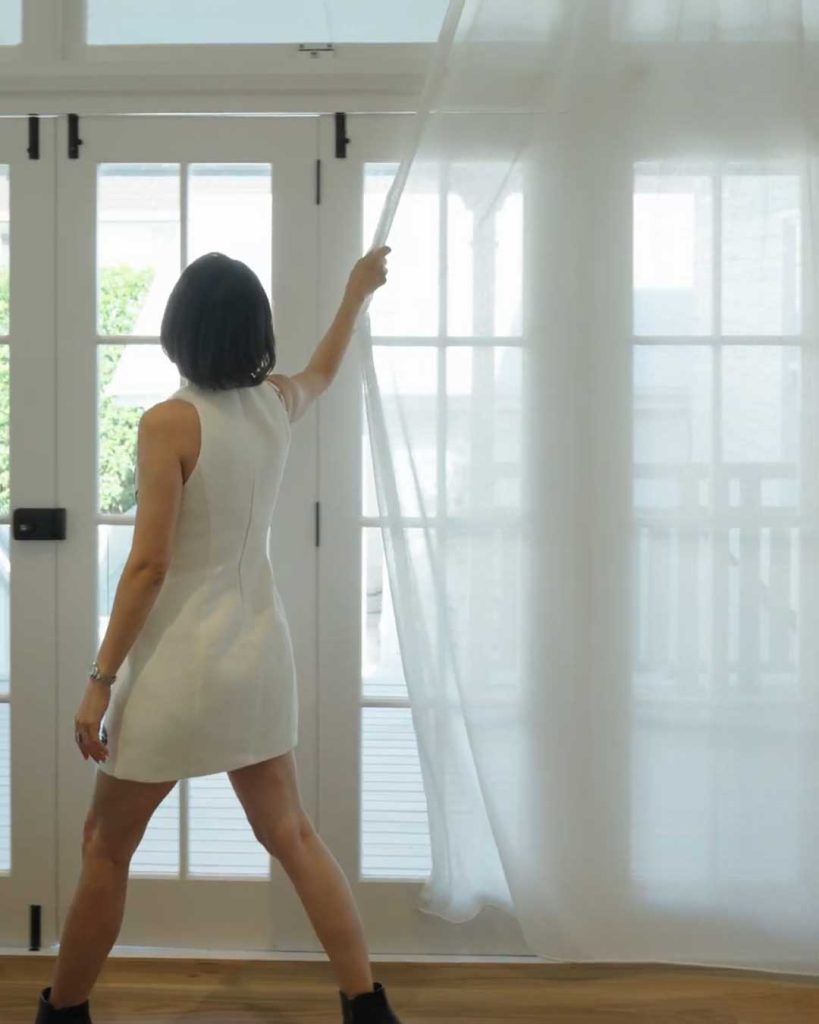 Woman opening sheer curtains in a bright living room
