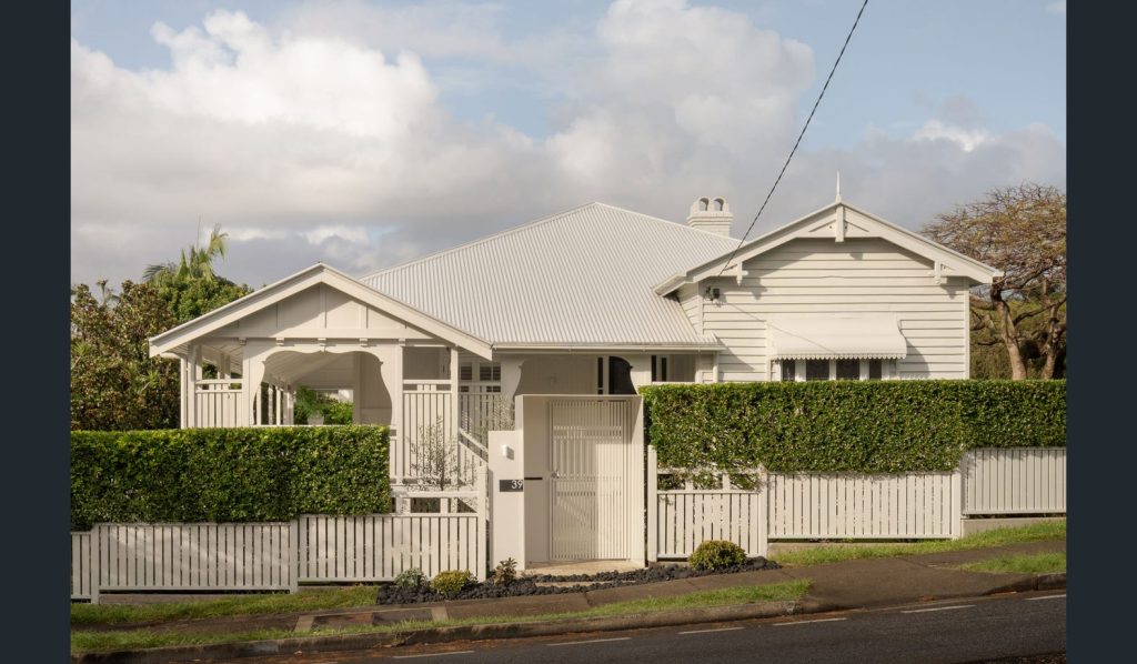 Traditional timber cottage behind a hedge and picket fence