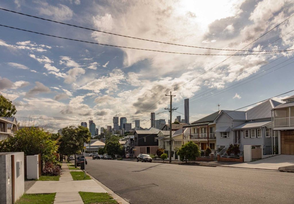 Street of timber homes with the Brisbane city skyline behind in New Farm